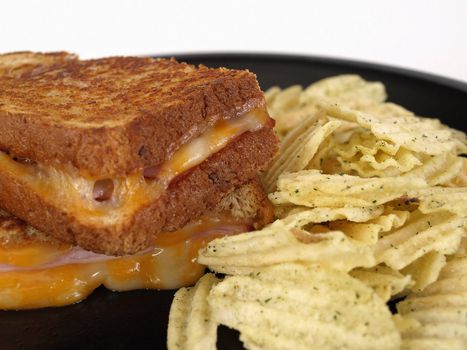 Hot maple ham and colby jack grilled cheese sandwich. On a black plate with seasoned potato chips.