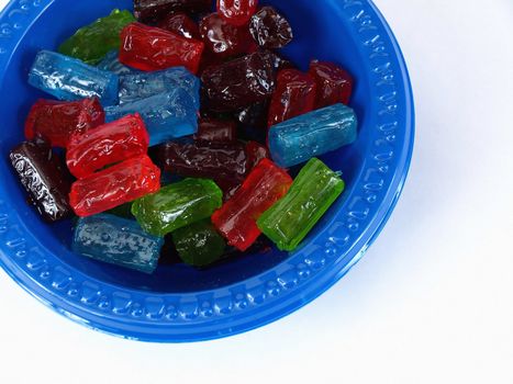 A blue plastic bowl full of colored hard candies. Over a white background.