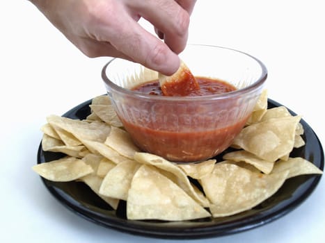 Male hand reaching out and dipping a corn chip in a bowl of salsa. Over a white background.