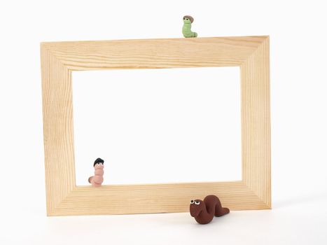 A blank tan wood frame set against a white background. Three Wermz are around and on the frame. Photographer holds copyright on figurines.