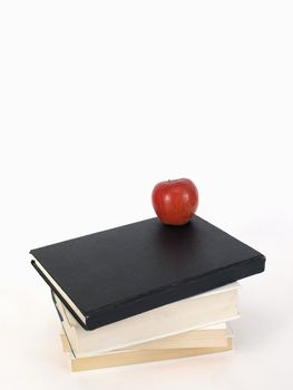 A stack of books and a ripe red delicious apple over a white background.