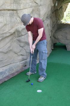 Handsome young man in tee-shirt and blue jeans playing a round of miniature golf.