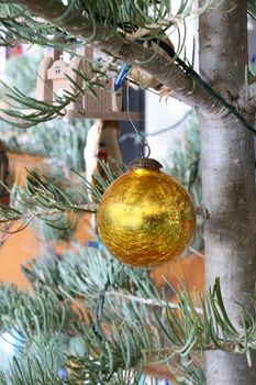 Golden, cracked glass Christmas ornament hanging on a Christmas tree.