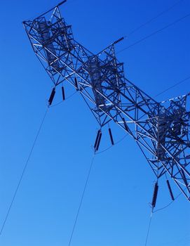 Electricity pylon taken from below looking up, diagonally across a bright blue sky