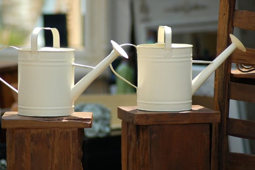 Pair of white metal watering cans on wooden podiums