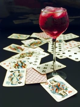 full of red wine and ice wineglass on the table with heap of plaing cards