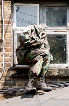 Headless mannequin with legs crossed, sitting on a window ledge, wearing army fatigues