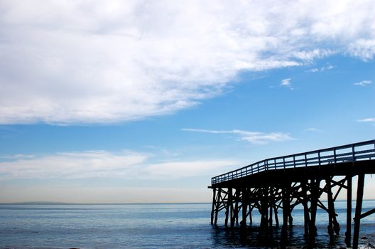Wooden pier. jetty into the ocean from the left hand side, into the ocean with a big blue cloudy sky