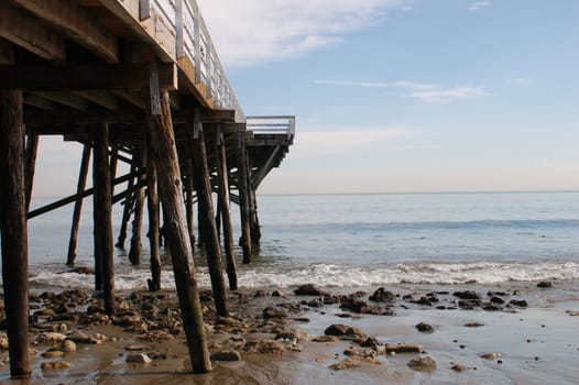 View out to sea from the right hand side of an old wooden pier, with wooden struts, rocks at the base, with the sea and sky merging in the distance