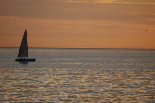 Landscape shot of a small sailboat against the horizon at sunset.