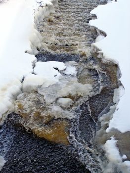 stream of water run through the snow and ice