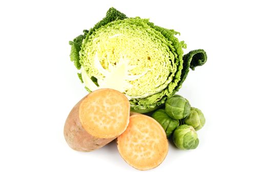 Half a raw green cabbage with a sweet potato cut in half and a pile of green sprouts on a reflective white background