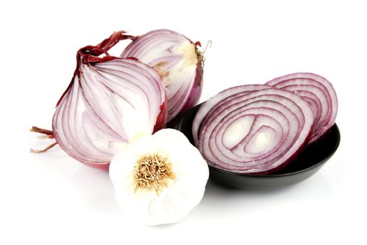 Raw red onion cut in half with slices in a dish and garlic on a reflective white background