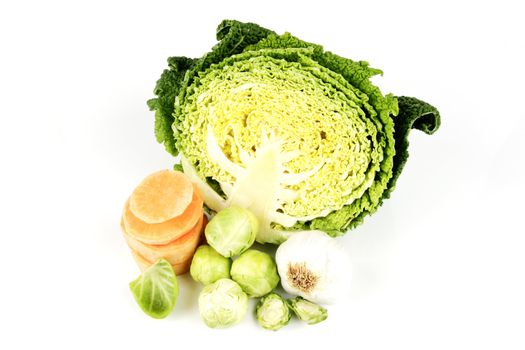 Half a raw green cabbage with garlic bulb, sprouts and slices of sweet potato on a reflective white background