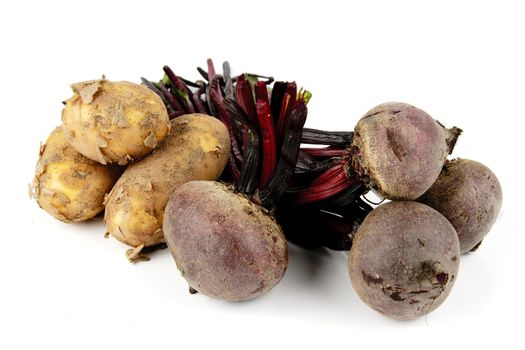 Bunch of raw red beetroot with a pile of small brown potatoes on a reflective white background