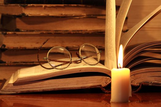 Closeup of candle with burning flame on background with old books and spectacles