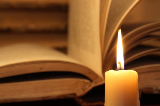 Closeup of candle with burning flame on vintage books background