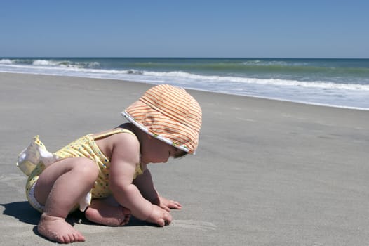 A baby plays with the sand during her first visit to the beach.