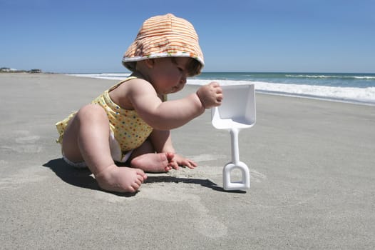 A baby plays with a shovel during her first visit to the beach.