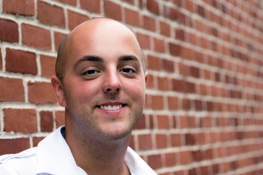 Portrait of a smiling bald young man posing in front of a brick wall.