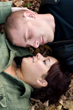 A young happy couple passionately kissing each other while laying in some autumn leaves.