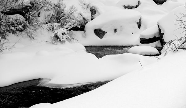 Snow drifts create unusual shapes over the boulders of a mountain river in Colorado.