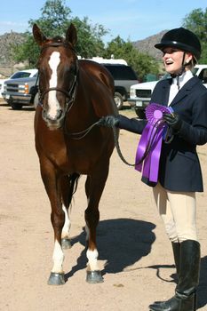 Young equestrian shows off her beautifully groomed horse and her champion rosette and blue ribbons.