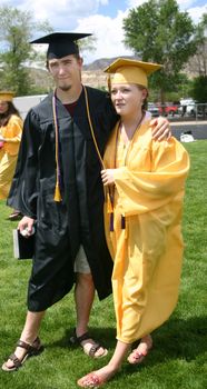 Attractive young couple in caps and gowns and sandals following their graduation ceremony.