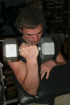 Young athlete is working on building biceps by working on curls with weights.