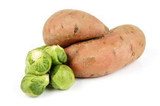 Two raw unpeeled sweet potatoes with a pile of green sprouts on a reflective white background