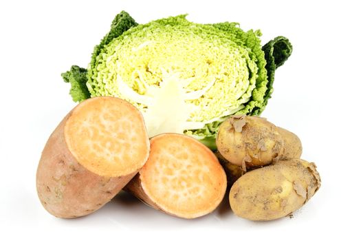 Half a raw green cabbage with a single sweet potato cut in half and a pile of brown potatoes on a reflective white background