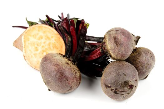 Bunch of raw red beetroot with a sweet potato cut in half on a reflective white background