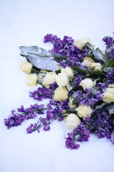 A flower arrangement in the snow, white roses and other blue flowers