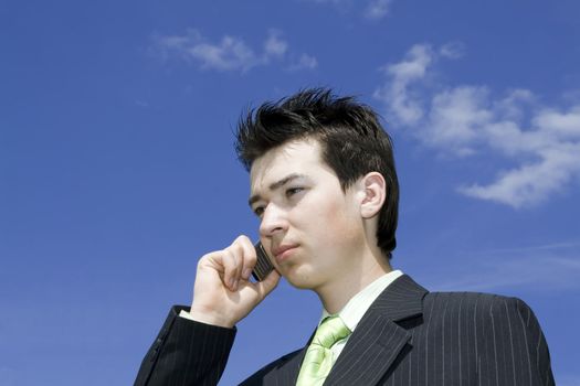 Businessman talking with mobile against blue sky background. Copyspace