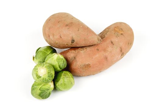 Two raw unpeeled sweet potatoes with a pile of green sprouts on a reflective white background