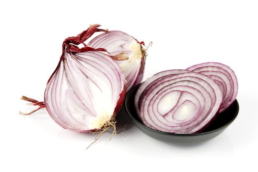 Raw red onion cut in half with slices in a small black dish on a reflective white background