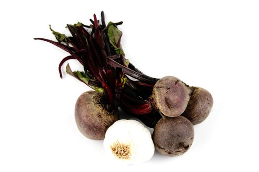Bunch of raw red beetroot with a small white bulb of garlic  on a reflective white background