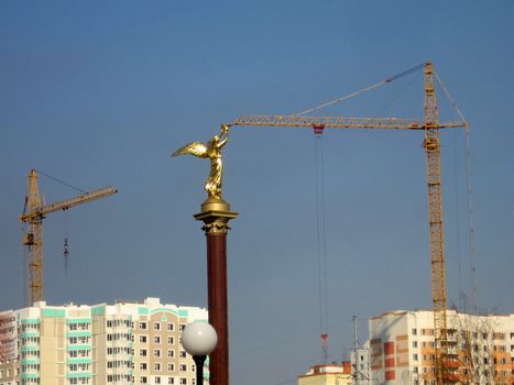 Gold statue reaches the crane on a background of new houses
