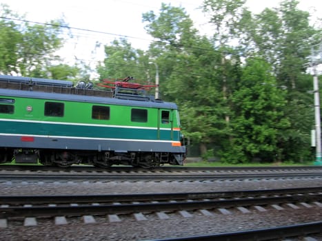 Green fast Russian locomotive moves through wood