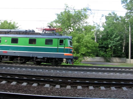 Green fast Russian locomotive moves through wood