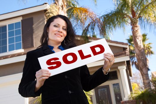 Happy Attractive Hispanic Woman Holding Sold Sign In Front of House.