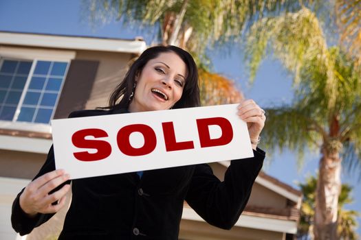 Happy Attractive Hispanic Woman Holding Sold Sign In Front of House.