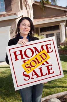 Happy Attractive Hispanic Woman Holding Sold Home For Sale Sign In Front of House.