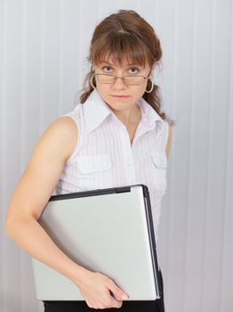 The serious girl holds the closed laptop in a hand
