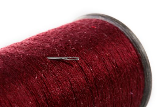 Darkly red threads and needle for sewing on a white background.