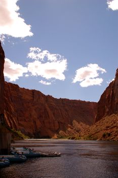 View of Colorado River just beyond the Glen Dam, in the Grand Canyon, with a few blue river rafts on the left and white clouds in a blue sky