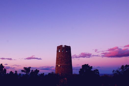 Rustic tower on the edge of the Grand Canyon, captured at sunset against a purple sunset with small clouds, in the centre of this landscape shot
