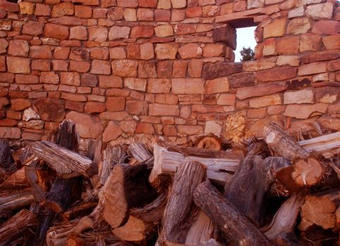 Rustic shot of an uneven hand built brick wall behind a large mound of chopped logs