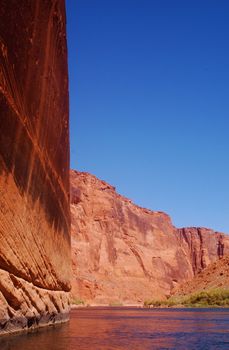 Incredible view from the Colorado River of the Grand Canyon with a vertical wall of red rock and still waters against a clear blue sky