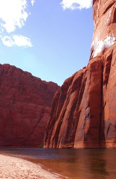 View from the Colorado River, looking up at the red rock walls of the Grand Canyon into a blue cloudy sky.